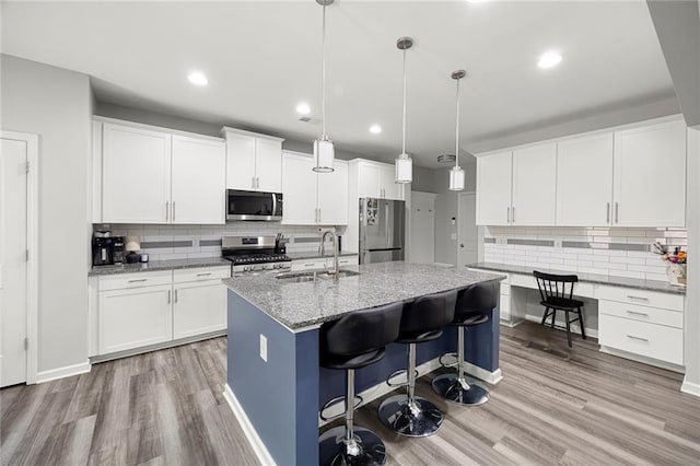 kitchen featuring appliances with stainless steel finishes, light stone counters, a sink, light wood-style flooring, and decorative backsplash