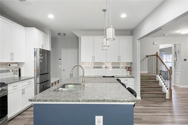 kitchen featuring white cabinetry, tasteful backsplash, light stone counters, a sink, and appliances with stainless steel finishes