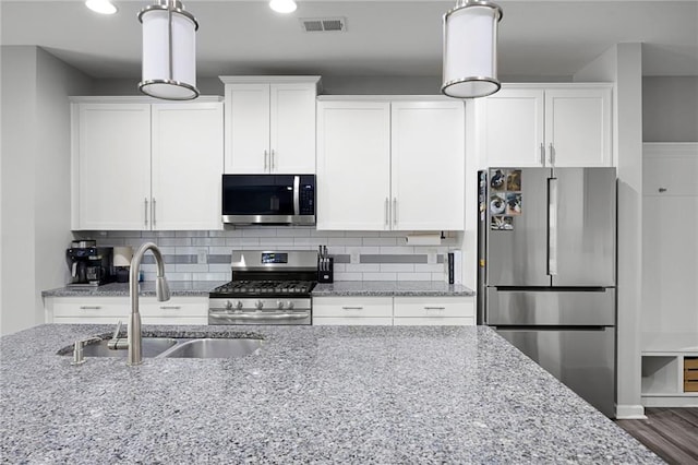 kitchen with light stone countertops, white cabinets, tasteful backsplash, a sink, and stainless steel appliances