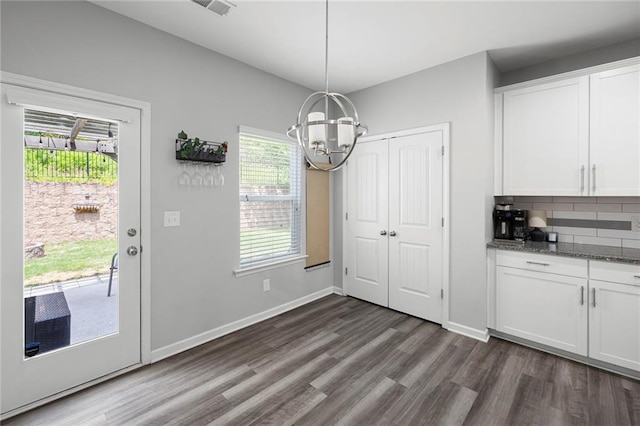 unfurnished dining area with baseboards, a notable chandelier, visible vents, and dark wood-type flooring