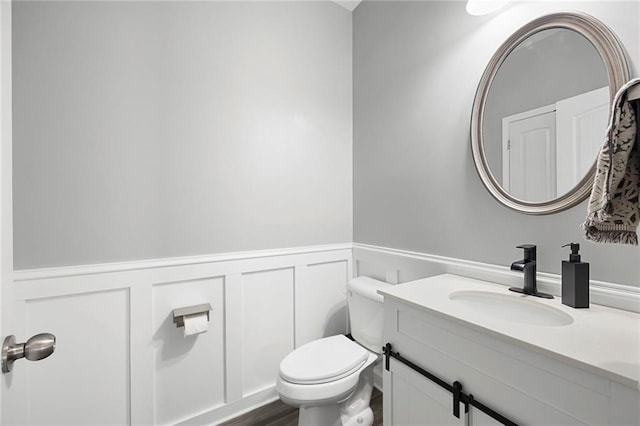 bathroom featuring vanity, a decorative wall, wainscoting, and toilet