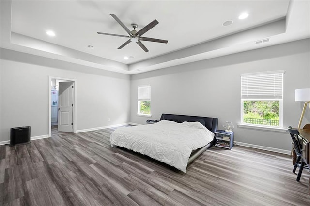 bedroom featuring a tray ceiling, visible vents, baseboards, and dark wood-type flooring
