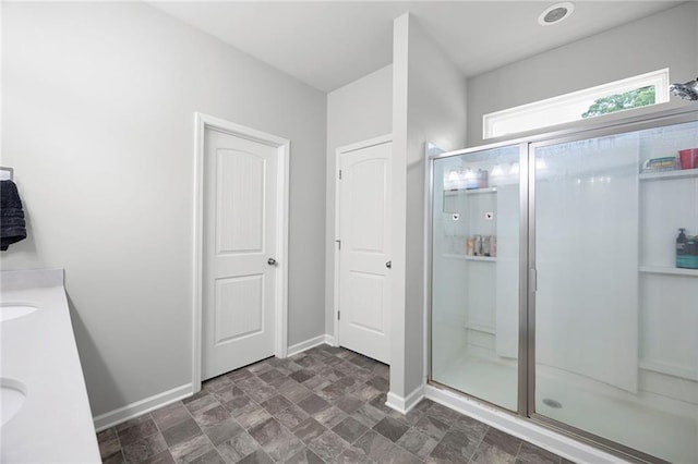 bathroom with baseboards, double vanity, a stall shower, and stone finish floor