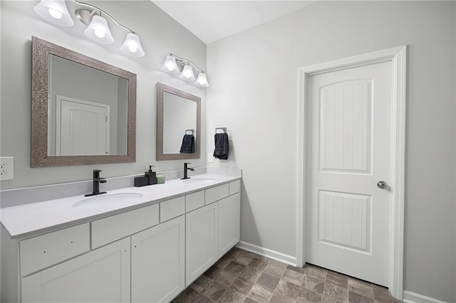 bathroom with baseboards, a sink, stone finish flooring, and double vanity