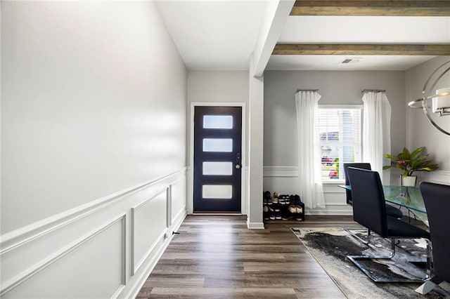 foyer entrance featuring dark wood-style flooring, visible vents, wainscoting, beam ceiling, and a decorative wall