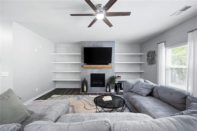 living room featuring a ceiling fan, baseboards, wood finished floors, a tile fireplace, and visible vents