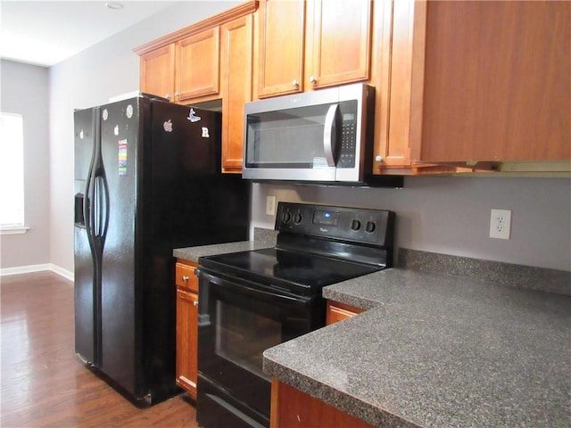 kitchen featuring dark countertops, black appliances, baseboards, and dark wood finished floors