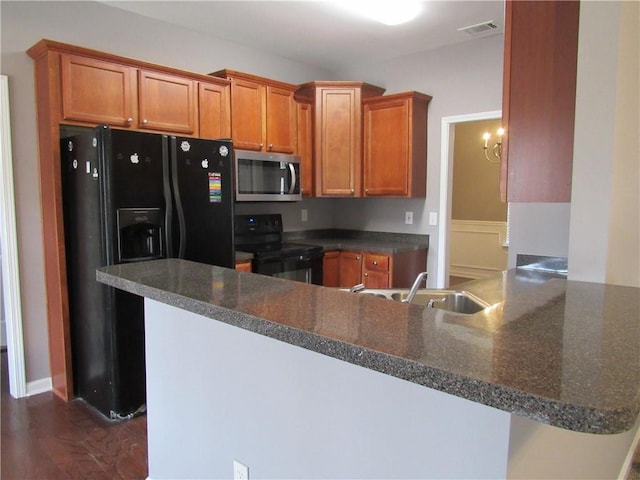 kitchen featuring visible vents, brown cabinetry, a sink, a peninsula, and black appliances