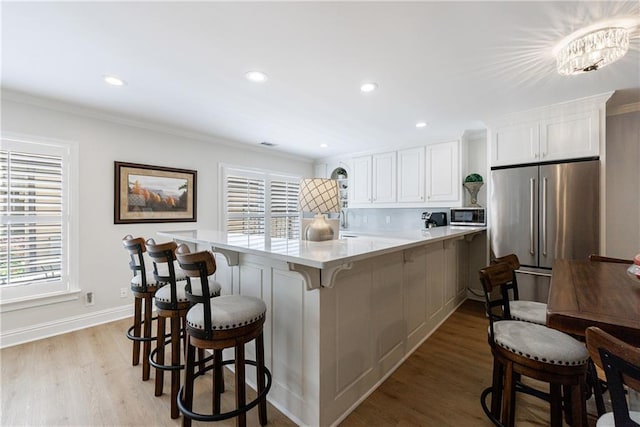 1021 Wetherby Way, Johns Creek, GA 30022 - kitchen with stainless steel appliances, a kitchen bar, light wood-style floors, white cabinets, and a peninsula
