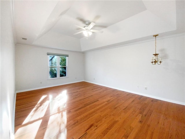 empty room with ceiling fan with notable chandelier, hardwood / wood-style flooring, and a tray ceiling