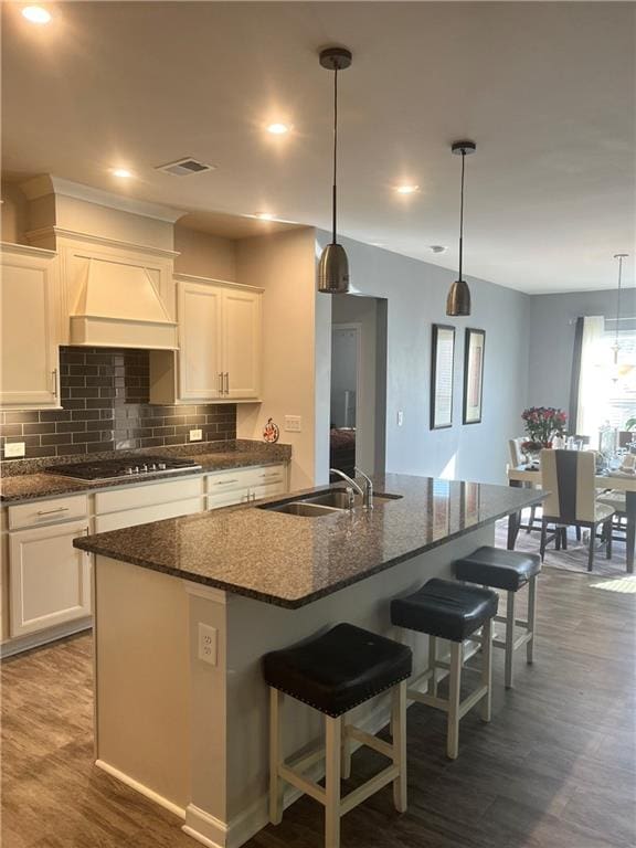 kitchen featuring gas cooktop, custom range hood, white cabinetry, and an island with sink