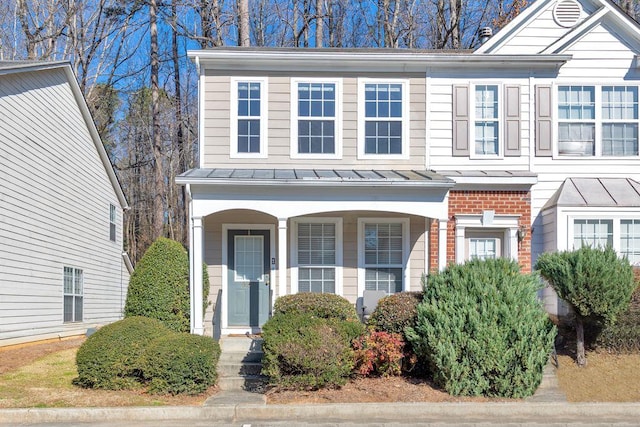 view of front of house featuring a standing seam roof, a porch, metal roof, and brick siding