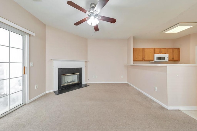 unfurnished living room with light carpet, a premium fireplace, a ceiling fan, and baseboards