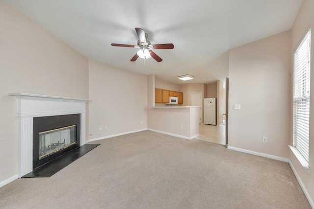 unfurnished living room with light carpet, plenty of natural light, baseboards, and a glass covered fireplace