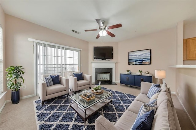 carpeted living area with ceiling fan, a fireplace with flush hearth, visible vents, and baseboards