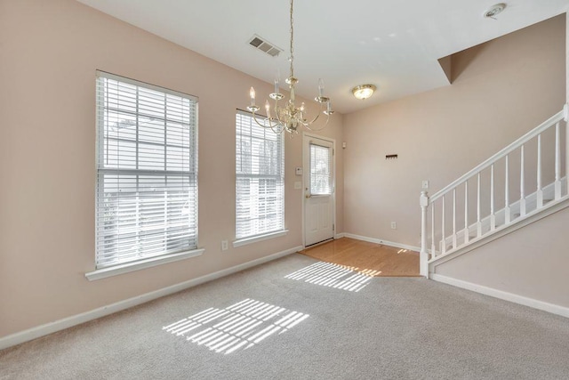 carpeted foyer entrance featuring a chandelier, visible vents, baseboards, and stairs