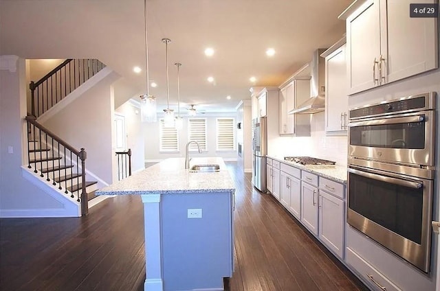 kitchen featuring a kitchen island with sink, sink, wall chimney exhaust hood, decorative light fixtures, and dark hardwood / wood-style flooring