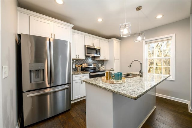 kitchen with appliances with stainless steel finishes, sink, white cabinets, light stone countertops, and a center island with sink