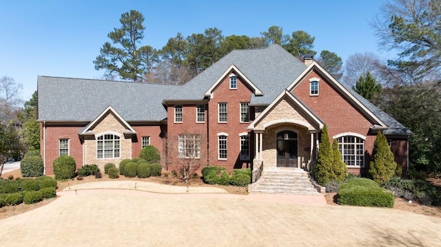 view of front of home with stone siding, brick siding, a chimney, and a shingled roof