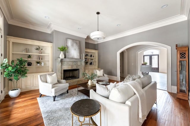 living room featuring arched walkways, a fireplace, crown molding, and wood finished floors