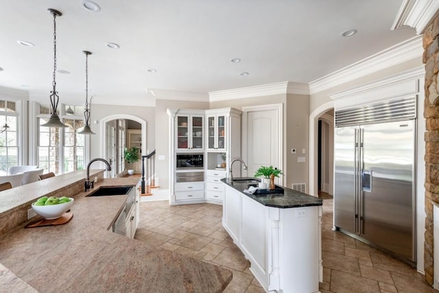 kitchen with stone tile flooring, appliances with stainless steel finishes, a kitchen island with sink, and a sink