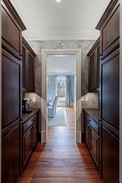 kitchen with crown molding, dark brown cabinets, dark wood-style floors, and dark stone counters