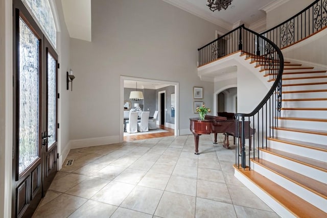 foyer entrance with stairway, baseboards, ornamental molding, a towering ceiling, and tile patterned floors