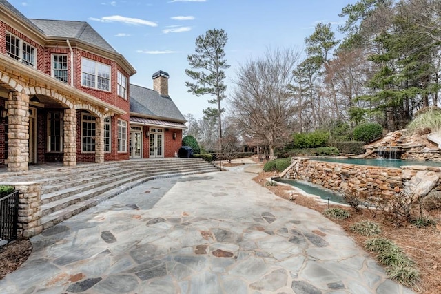 view of side of home featuring french doors, brick siding, a chimney, and a patio area