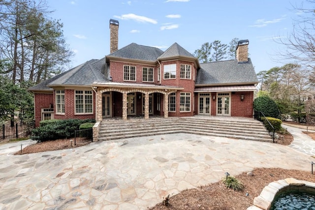 rear view of house with brick siding, french doors, fence, and a chimney