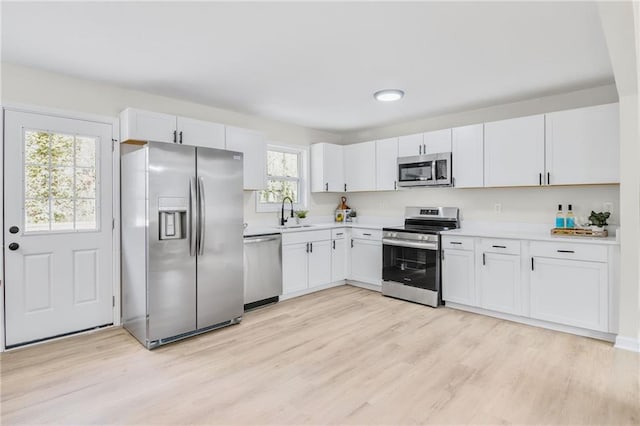 kitchen featuring stainless steel appliances, sink, light hardwood / wood-style flooring, and white cabinets