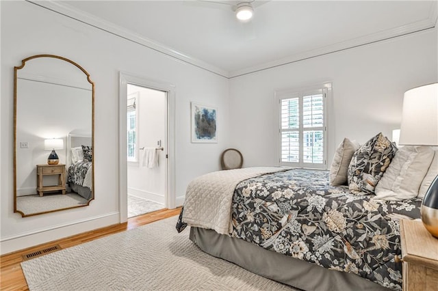 bedroom featuring wood finished floors, visible vents, ornamental molding, baseboards, and ensuite bathroom
