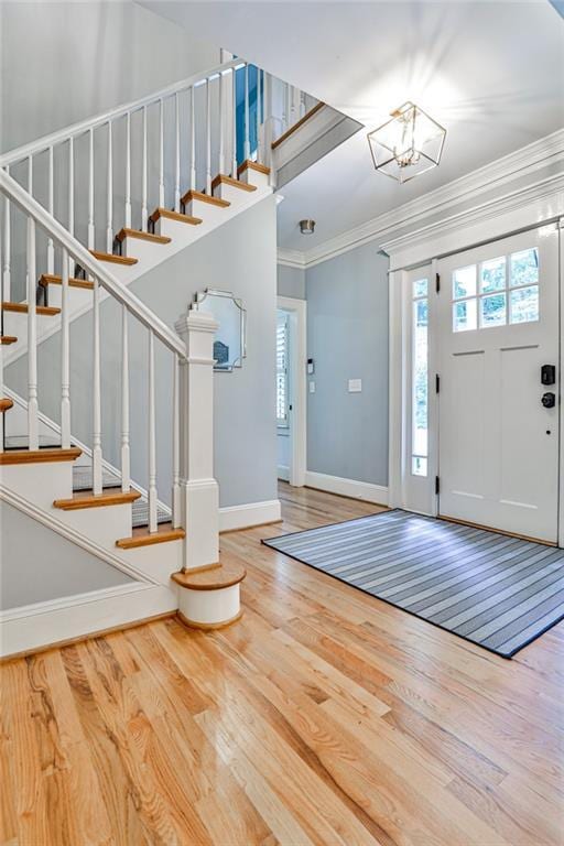 entryway with baseboards, a notable chandelier, wood finished floors, stairway, and crown molding