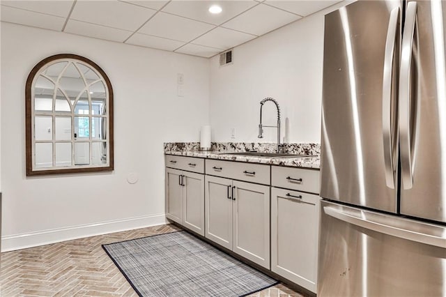 kitchen featuring visible vents, a sink, freestanding refrigerator, brick floor, and baseboards