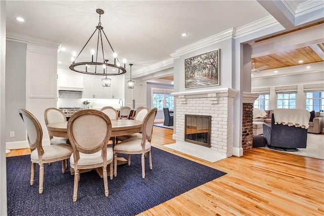 dining space with wood finished floors, a brick fireplace, ornamental molding, and ceiling fan with notable chandelier