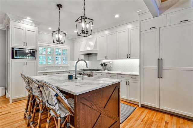 kitchen featuring premium range hood, stainless steel microwave, an inviting chandelier, and light wood-style floors