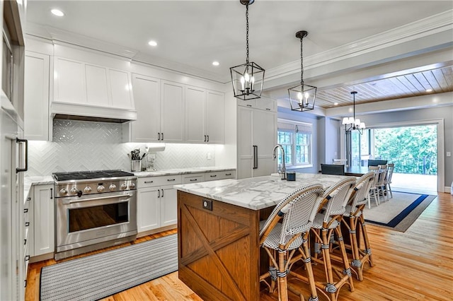 kitchen featuring a notable chandelier, backsplash, light stone countertops, stainless steel range, and white cabinetry