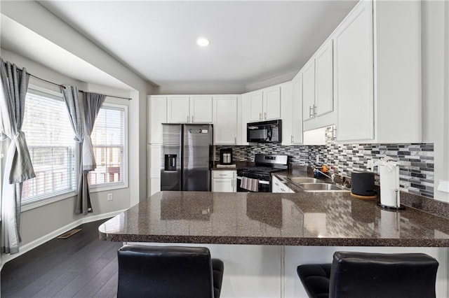 kitchen featuring stainless steel appliances, a peninsula, a sink, white cabinetry, and tasteful backsplash