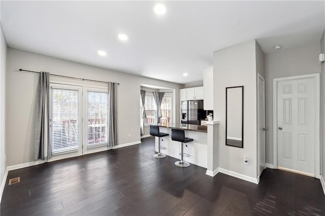 kitchen with a peninsula, dark wood-style flooring, a kitchen breakfast bar, white cabinets, and stainless steel fridge with ice dispenser