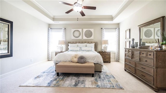 bedroom with a raised ceiling, light colored carpet, baseboards, and multiple windows