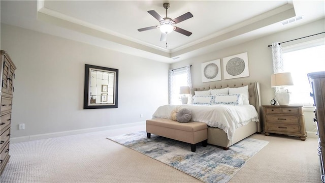 bedroom with visible vents, a tray ceiling, baseboards, and light carpet