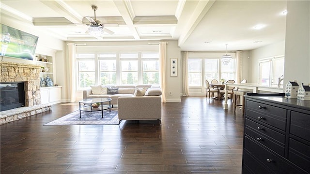 living area with baseboards, a stone fireplace, a ceiling fan, dark wood-type flooring, and beamed ceiling