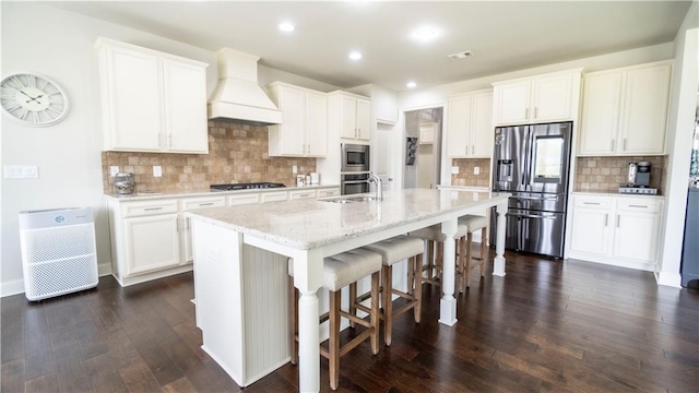 kitchen featuring custom exhaust hood, dark wood-style flooring, a kitchen breakfast bar, appliances with stainless steel finishes, and a sink