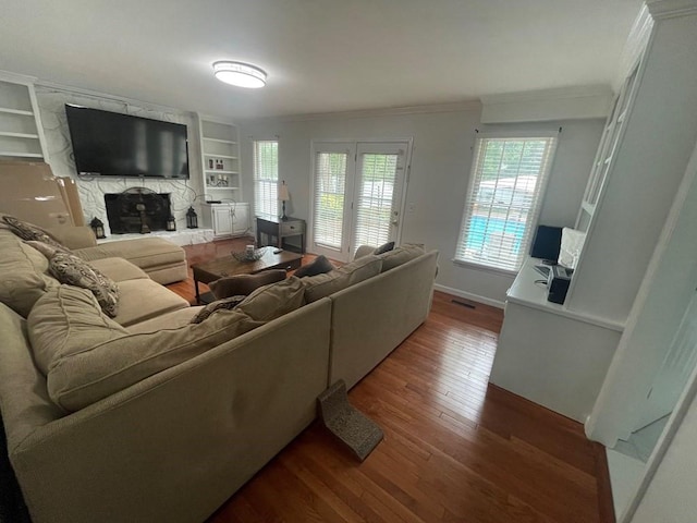 living room featuring built in features, wood-type flooring, ornamental molding, and a stone fireplace