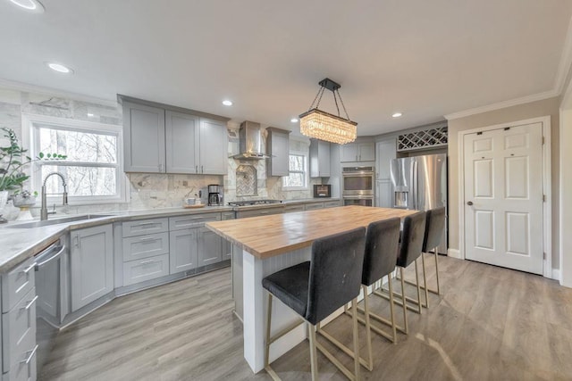 kitchen featuring a center island, wall chimney exhaust hood, stainless steel appliances, wooden counters, and pendant lighting