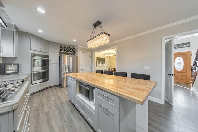 kitchen with gray cabinetry, a center island, hanging light fixtures, stainless steel appliances, and wood counters