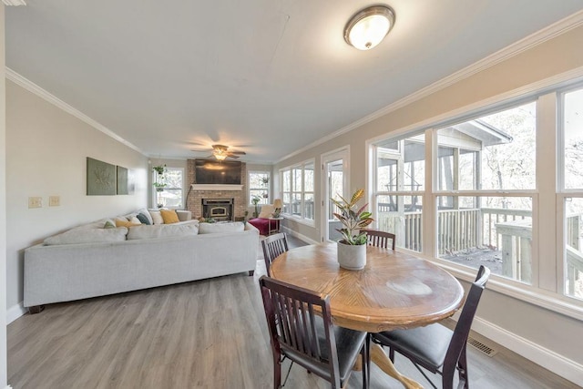 dining room with a brick fireplace, light hardwood / wood-style flooring, ceiling fan, and crown molding