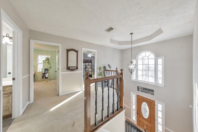 interior space featuring a raised ceiling, light colored carpet, a textured ceiling, and a notable chandelier