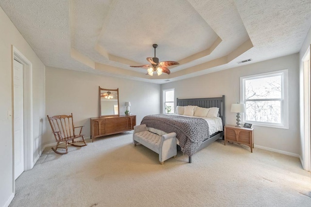 bedroom featuring a raised ceiling, ceiling fan, light carpet, and a textured ceiling