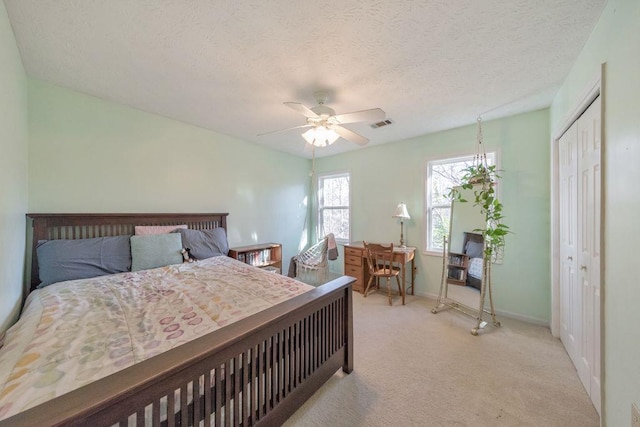 bedroom with ceiling fan, a closet, light colored carpet, and a textured ceiling