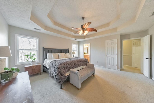 bedroom with a textured ceiling, light colored carpet, a raised ceiling, and ceiling fan